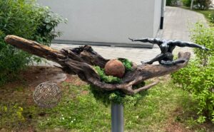Gartendeko: Skulptur auf Holz mit Mann, Moos, Kugel. Kunstvolle Gartengestaltung. Naturmaterialien.