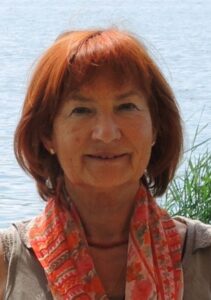 Porträt einer reifen Frau mit roten Haaren und Schal vor einem See.
