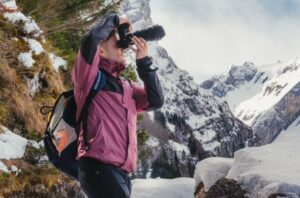 Bergfotograf mit Kamera in verschneiter Alpenlandschaft. Wanderer macht Fotos von Bergen.