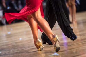 Paartanz: Füße und Beine von Tänzern in Bewegung. Rotes Kleid, goldene Tanzschuhe, schwarze Hose.