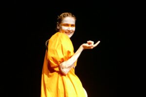 Frau mit orangefarbenem Kleid und Gesichtsbemalung auf der Bühne. Theateraufführung.