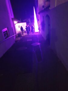 Gasse bei Nacht mit lila Licht. Menschengruppe im Hintergrund. Architektur und Beleuchtung.