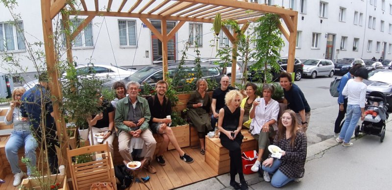Gruppe von Menschen sitzt im Freien unter einer Holzpergola mit Pflanzen. Urban Gardening.