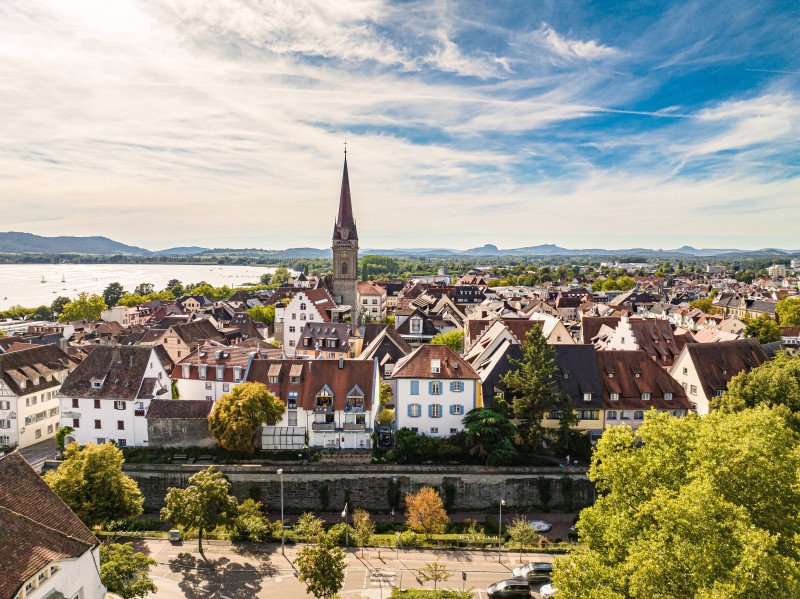 event-a02a9fcd-4cad-4b62-bfec-a946324c4a0d-1 Überblick über Radolfzell am Bodensee mit Kirchturm und Seeufer. Stadtansicht, Tourismus.