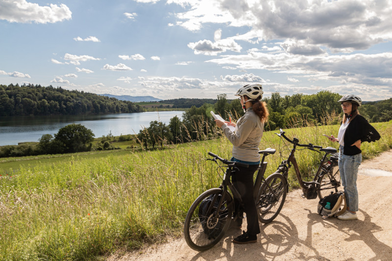 Zwei Frauen mit Fahrrädern und Helmen am See. Radfahren, Natur, Ausflug.