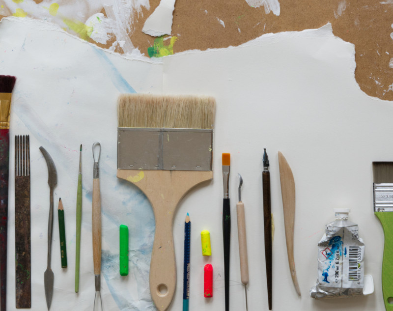 Kreatives Chaos: Pinsel, Farben, Stifte und Malwerkzeuge auf Papier. Künstlerbedarf für Malerei und Kunstprojekte.