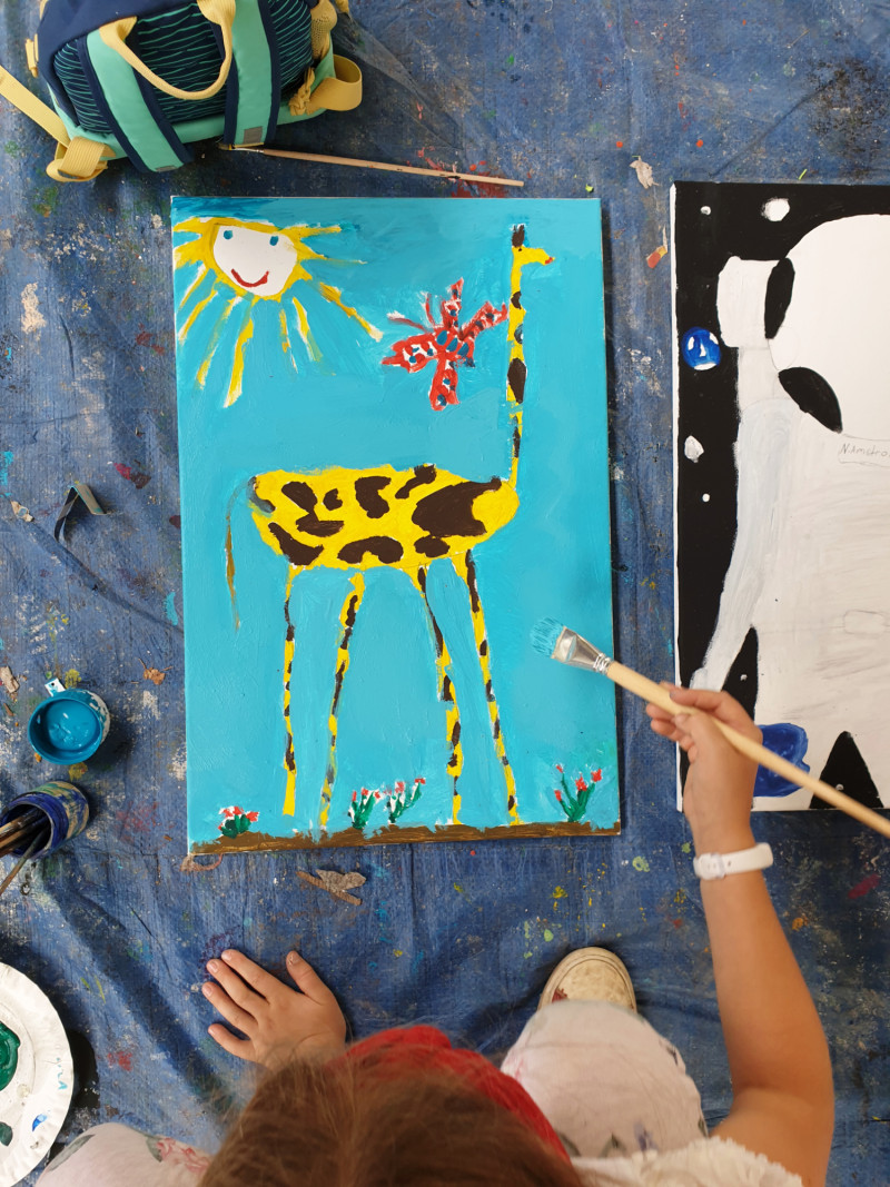 Mädchen malt Giraffe auf Leinwand mit Sonne und Schmetterling, kreatives Kinderkunstprojekt.