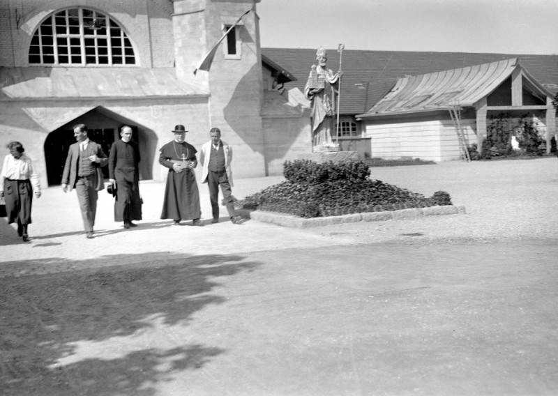 Historisches Schwarzweißfoto: Gruppe von Personen vor Gebäude mit Heiligenstatue, vermutlich Kirche. Religiöses Motiv.