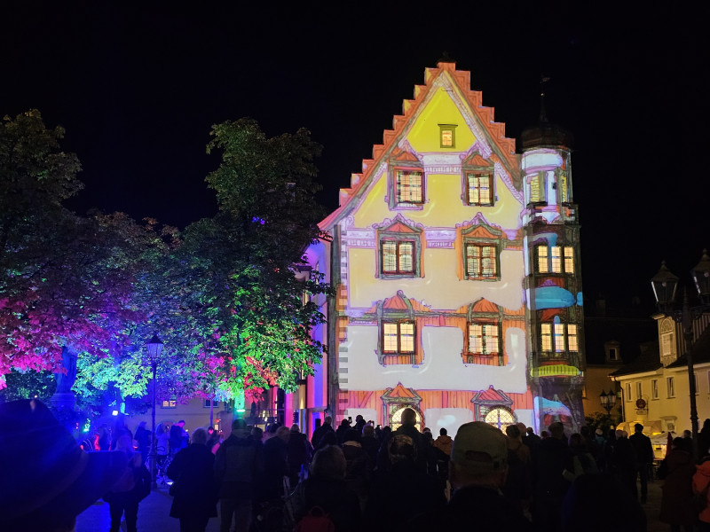 Illuminierte Fassade in Deutschland: Farbenfrohe Lichtprojektion auf historischem Gebäude, Menschenmenge im Vordergrund.